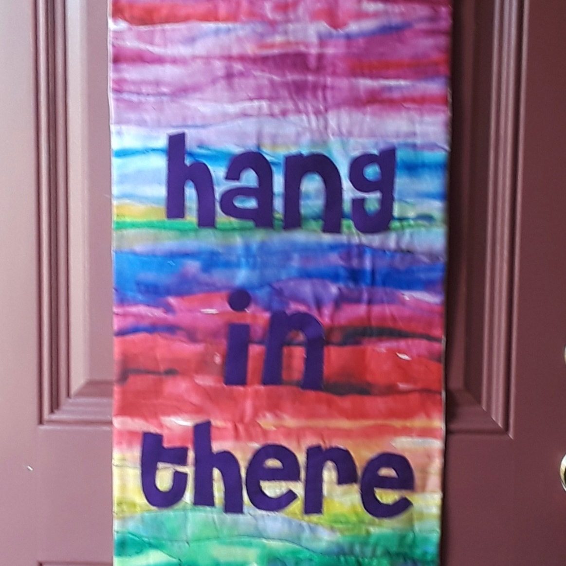multi-colored quilted banner hanging on interior door, text: hang in there